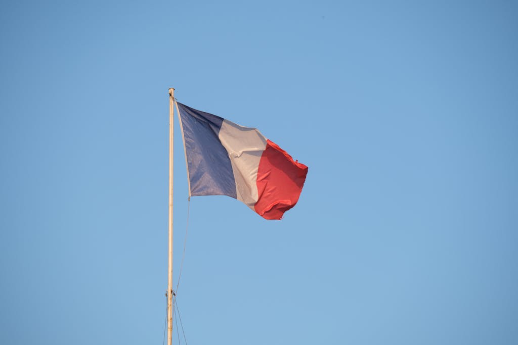 The French national flag waving on a flagpole against a clear blue sky.