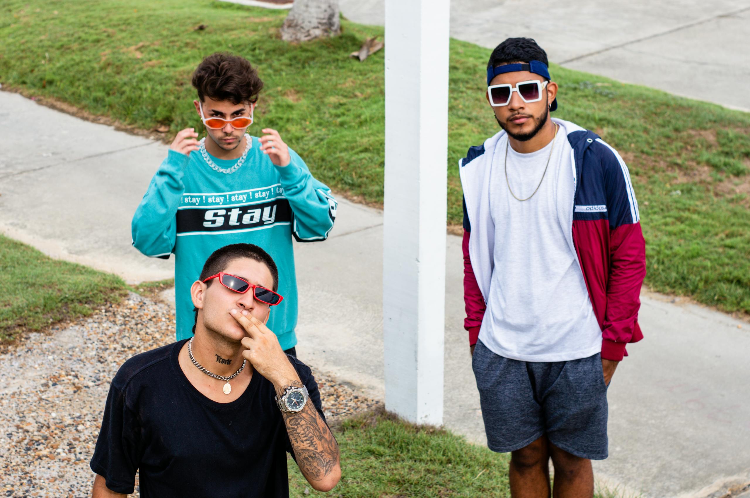 Three young men in stylish outfits and sunglasses pose on a sidewalk in Cartagena, Colombia.